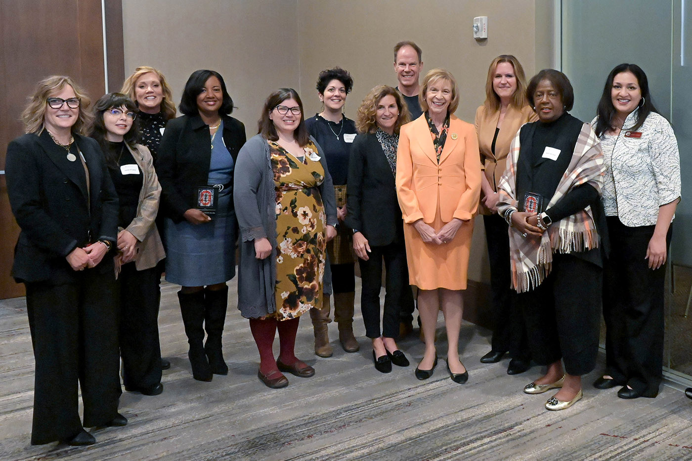 A group photograph of the speakers and award winners at the 2023 Crane Center Symposium on Children. There are 12 individuals in the photograph, all of whom are looking at the camera and smiling.