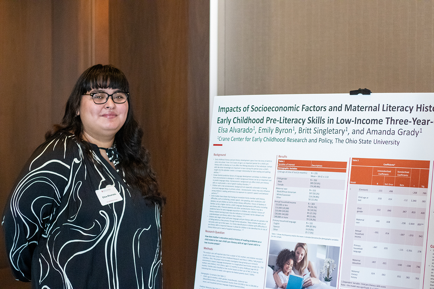 Elsa Alvarado stands next to a poster describing research in which she participated on the impacts of socioeconomic factors and maternal literacy history on early childhood pre-literacy skills in low-income three-year-olds. The poster was displayed at the 2023 Symposium on Children.