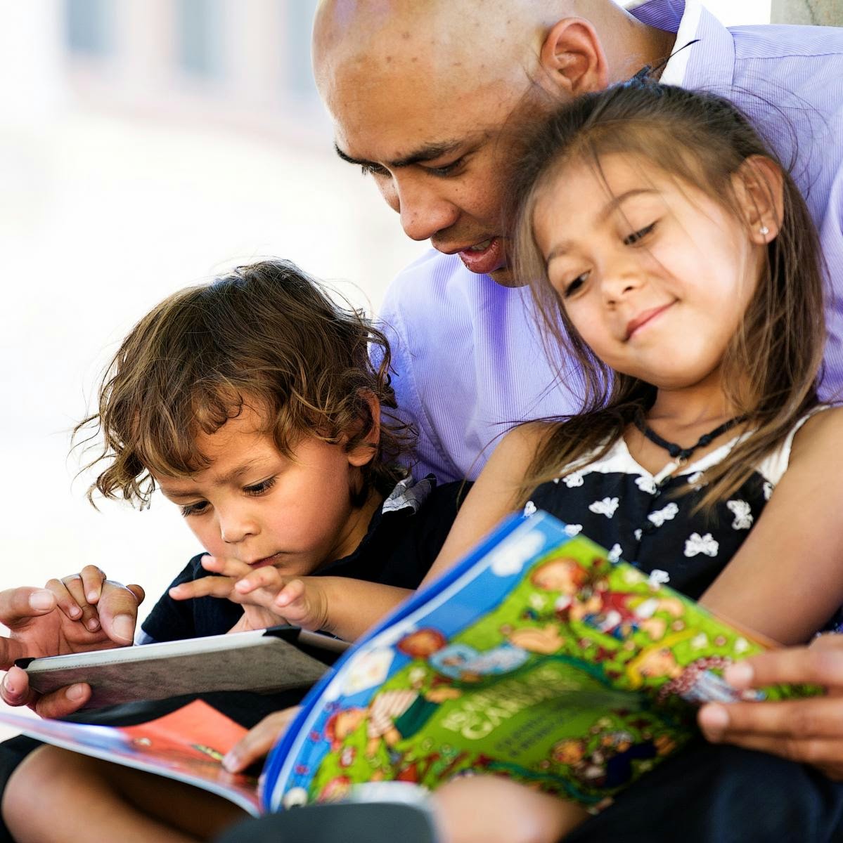 A man sits with two small children in his lap, each child holding an open book.