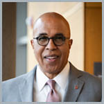 Dean Pope-Davis smiles at the camera in a gray suit with pink tie.