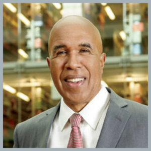 Dean Pope-Davis smiles at the camera in a gray suit with pink tie.