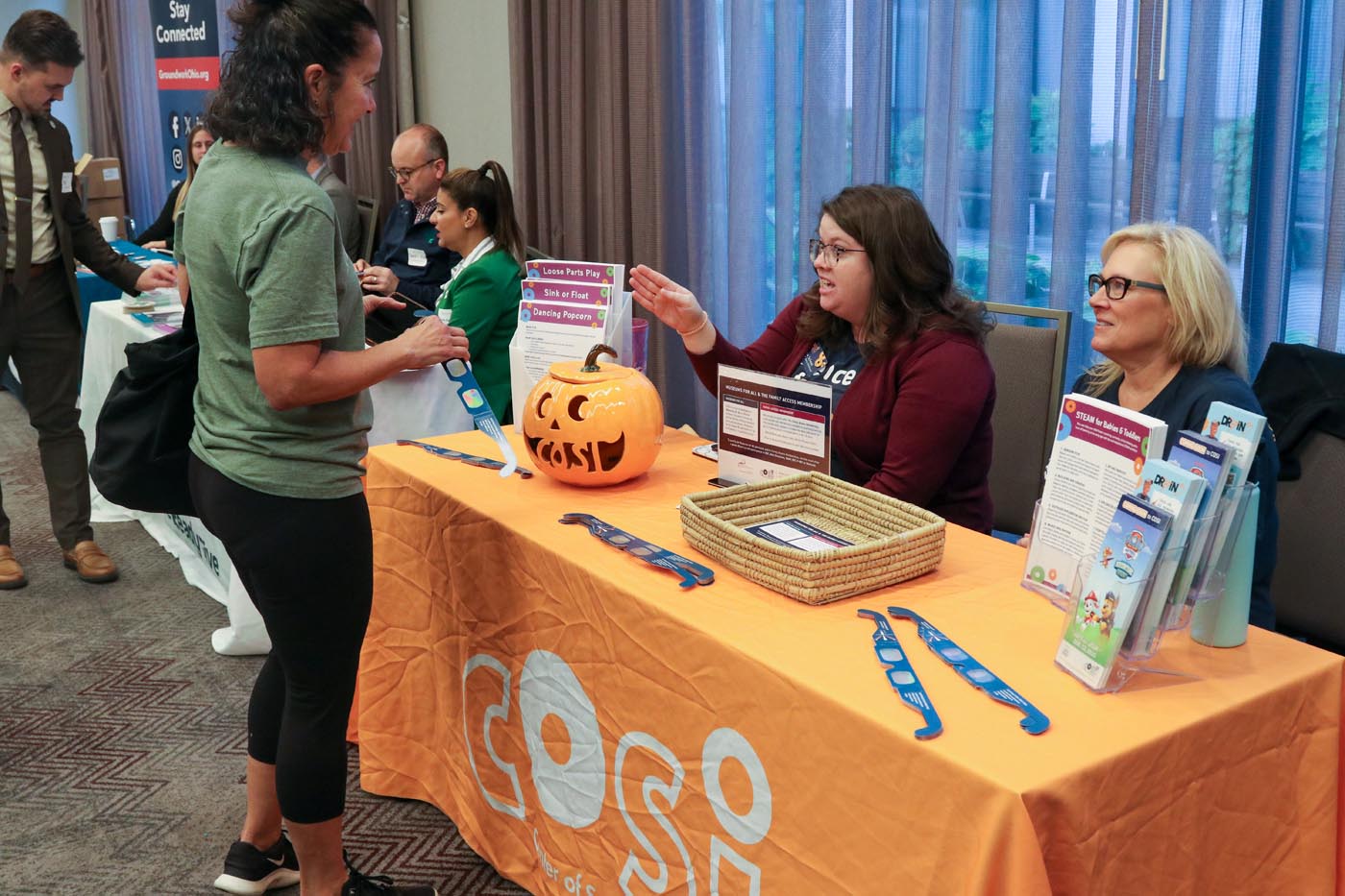 A table from the COSI science museum had a toy ceramic pumpkin on display, along with paper solar glasses that children can use to learn about science.