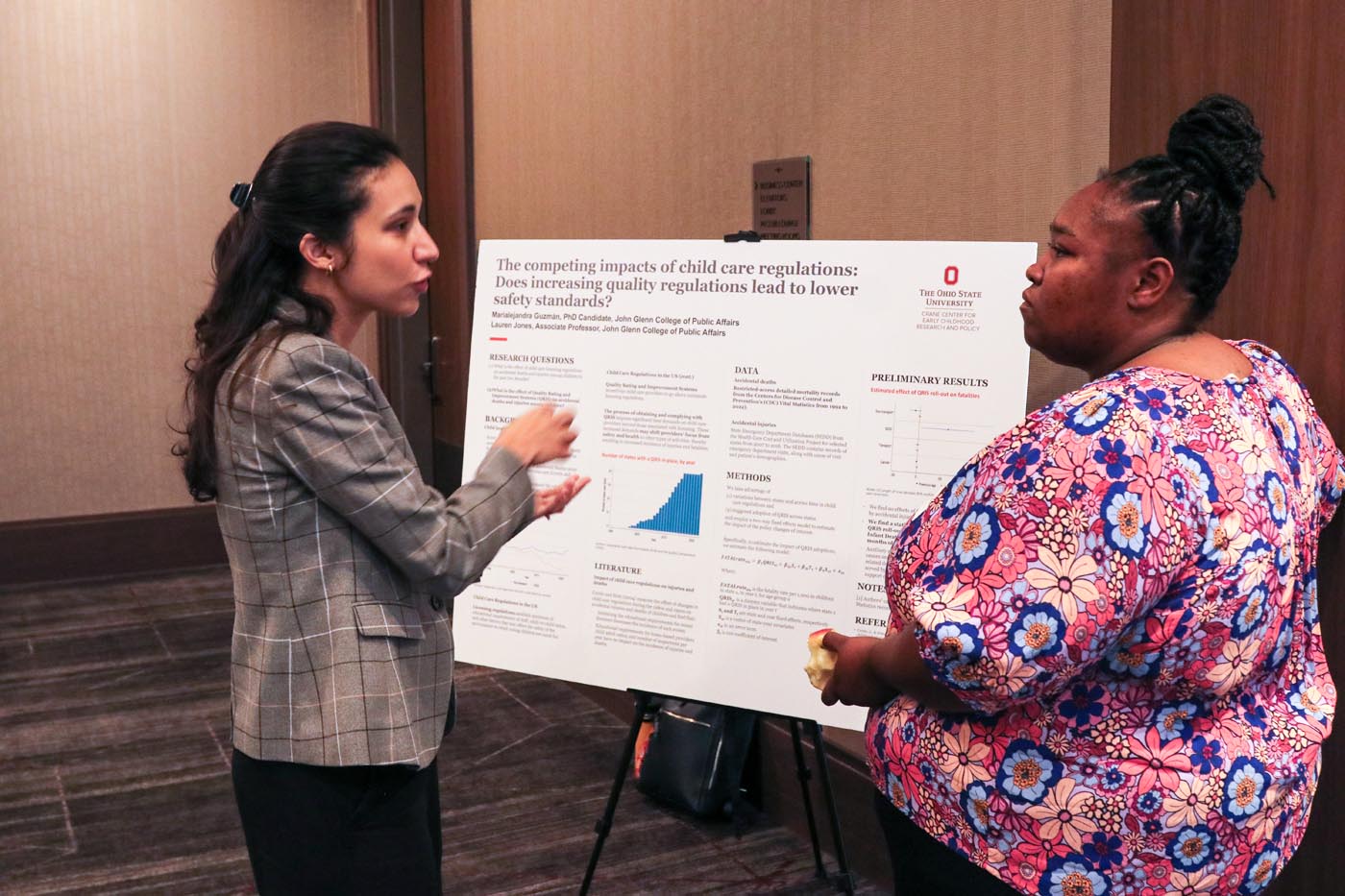 Two women stand in front of a poster showing research results.