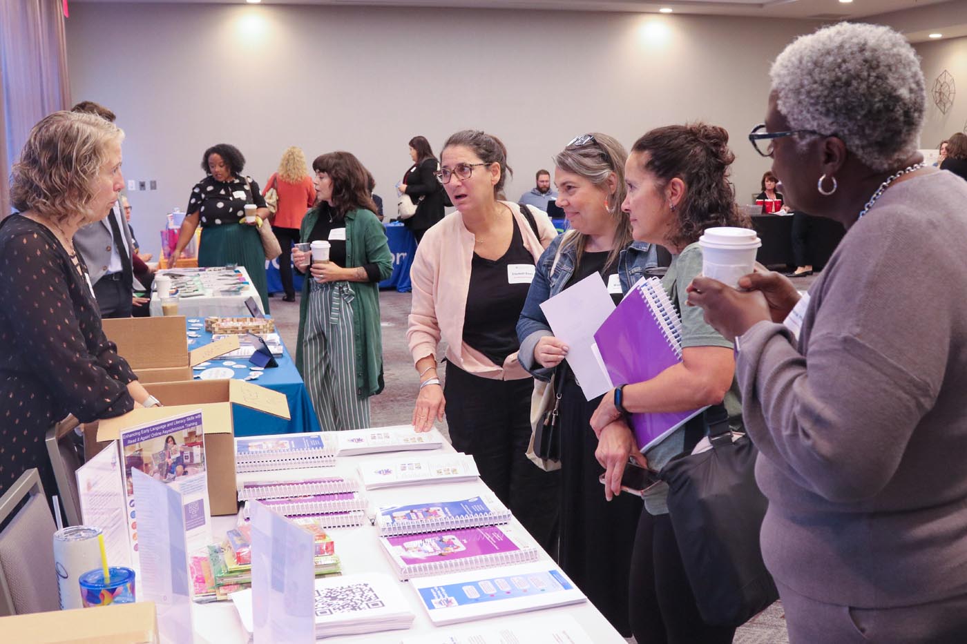 Attendees surround a display table with paper handouts.