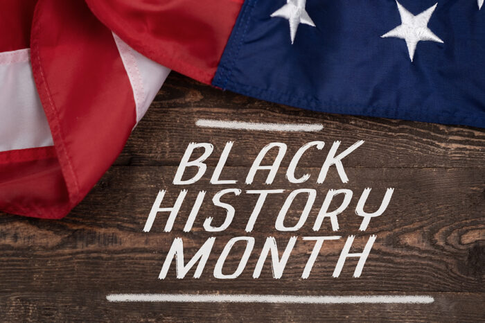 A section of an American flag lies on a wooden background. Over the wooden background are written the words "BLACK HISTORY MONTH."