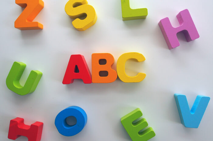 A group of painted wooden block letters rest on a white background. In the center of the image, the letters ABC appear, surrounded by other random letters.